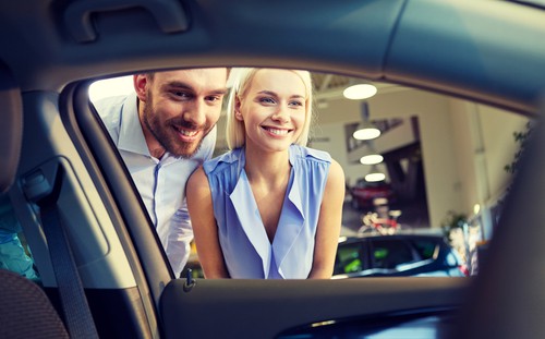 a couple looks through the window of a vehicle while searching to buy a car
