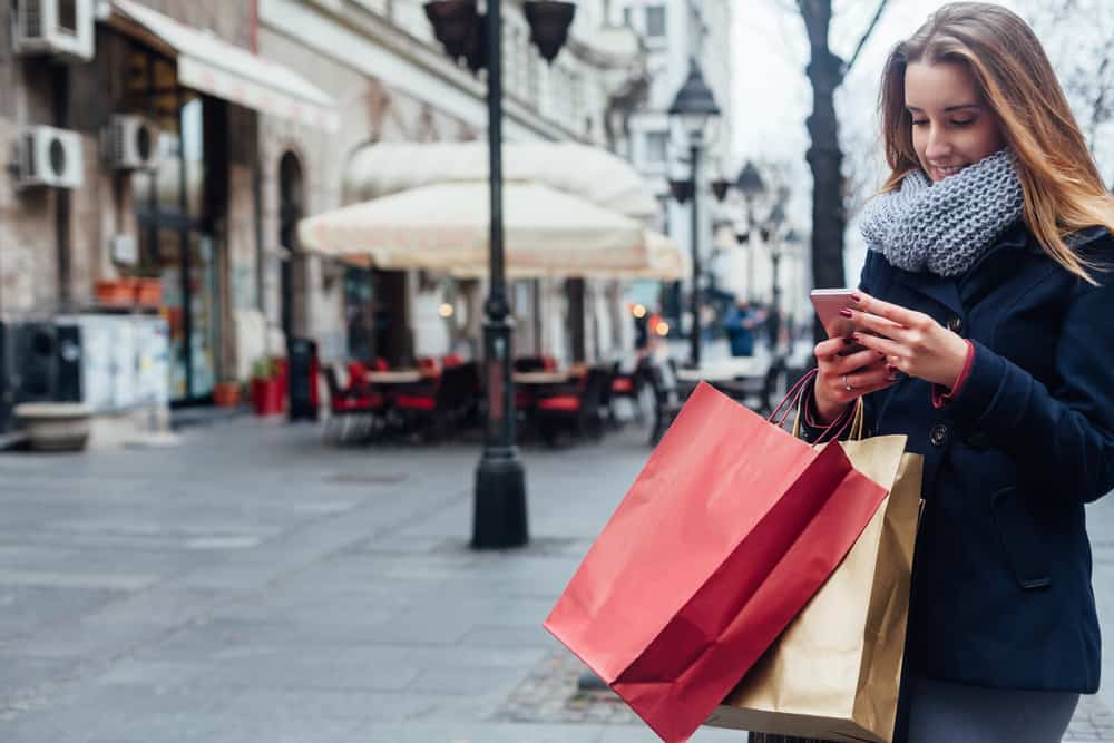 A woman looks at her mobile phone while she holds shopping bags